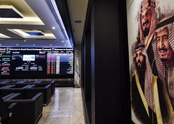 This picture taken December 12, 2019 shows (L) a view of the exchange board at the Stock Exchange Market (Tadawul) bourse in Riyadh displaying Aramco shares on the second day of their trading, along with a poster depicting Saudi Arabia's founder King Abdulaziz ibn Saud (C), his son and current King Salman bin Abdulaziz (R), and the latter's son Crown Prince Mohammed bin Salman (L) on display. - Energy giant Saudi Aramco's market value soared above $2 trillion as its share price surged again on its second day of trading. The valuation milestone was sought by Saudi Crown Prince Mohammed bin Salman when he first floated the idea of selling up to five percent of Aramco, the world's largest oil firm, about four years ago. Aramco shares jumped another 9.7 percent to 38.60 riyals ($10.3) on Thursday morning, following a 10-percent rise the previous day. (Photo by FAYEZ NURELDINE / AFP)