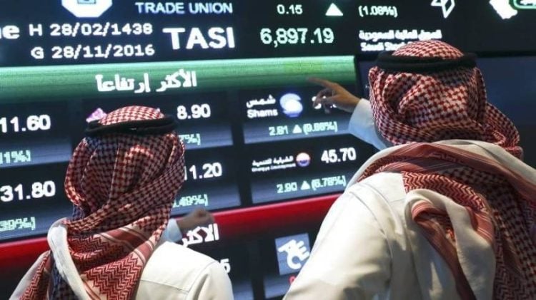 Visitors stand and watch stock movements displayed on large video screens inside the Saudi Stock Exchange, also known as the Tadawul All Share Index in Riyadh, Saudi Arabia, on Monday, Nov.28, 2016. The Tadawul All Share Index advanced 26 percent since Saudi Arabias record-breaking bond sale last month, the most in the world during that period. Photographer Simon Dawson/Bloomberg