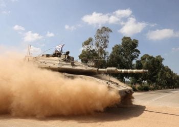 An Israeli army Merkava battle tank crosses a street while moving in a convoy along the border with the Gaza Strip in southern Israel on October 13, 2023. Thousands of people, both Israeli and Palestinians have died since October 7, 2023, after Palestinian Hamas militants entered Israel in a surprise attack leading Israel to declare war on Hamas in the Gaza Strip enclave on October 8. (Photo by Menahem KAHANA / AFP)