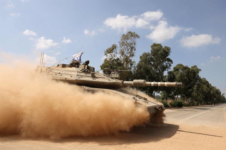 An Israeli army Merkava battle tank crosses a street while moving in a convoy along the border with the Gaza Strip in southern Israel on October 13, 2023. Thousands of people, both Israeli and Palestinians have died since October 7, 2023, after Palestinian Hamas militants entered Israel in a surprise attack leading Israel to declare war on Hamas in the Gaza Strip enclave on October 8. (Photo by Menahem KAHANA / AFP)