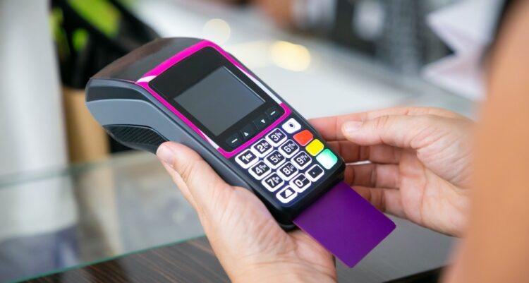 Clothes store cashier operating payment process with pos terminal and credit card. Cropped shot, closeup of hands. Shopping or purchase concept